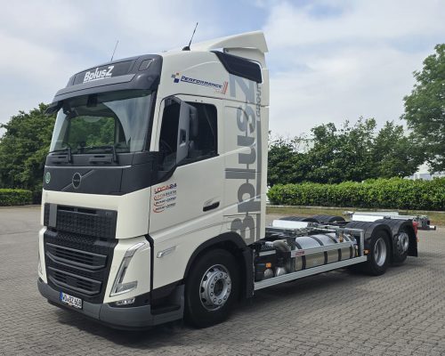 Weißes Volvo FH BDF-Wechselfahrgestell der BplusZ Group mit grauem Firmenlogo, geparkt auf einem gepflasterten Gelände vor grünem Hintergrund.